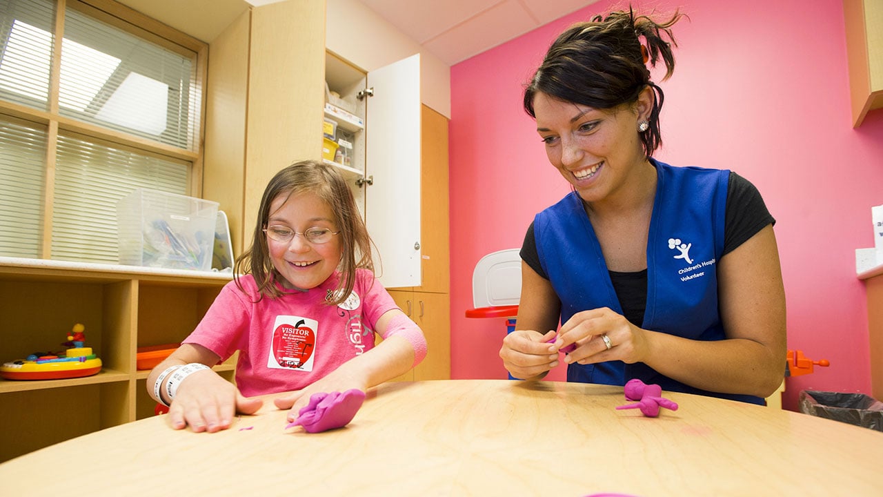 A volunteer donates her time to play with play-doh with a girl patient.