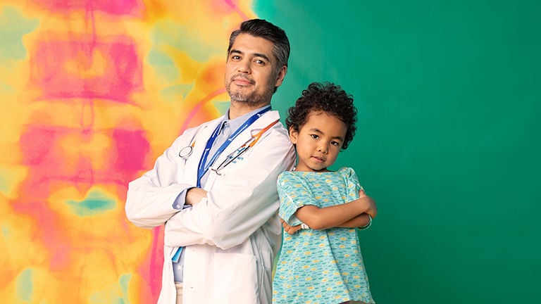 A doctor and a young patient stand facing the camera with their arms crossed