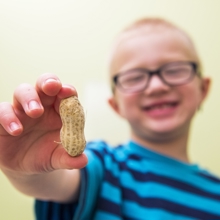 A boy with glasses holds up a peanut