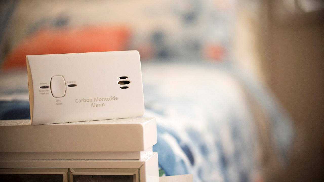 A white carbon monoxide detector sits on the edge of a bed.