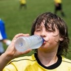 A boy in a yellow jersey drinks from a water bottle at a soccer field.