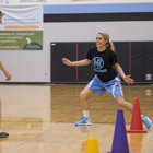 A Sports Medicine Center physical therapist stands in a gym, helping a teenage athlete recover from her sports injury.