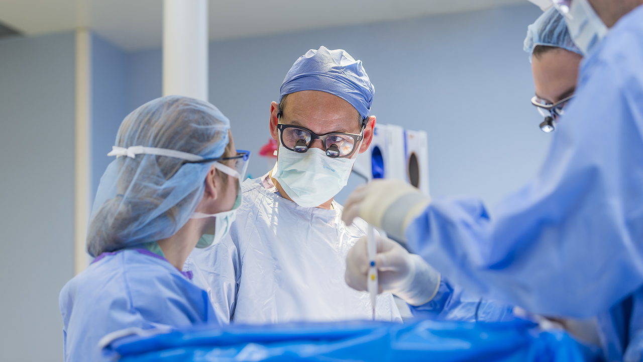 This is a picture of a surgeon performing surgery in the OR with three other healthcare professionals. 